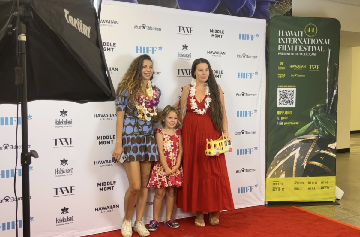 A promotional sign for HIFF is displayed past the concession area at Consolidated Theatres in Kahala Mall, as two actresses and a young girl pose for photos at the HIFF-branded media wall featuring sponsors like Star Advertiser, Hawaiian Airlines, Halekulani, Middle Management and the Asian American Foundation.